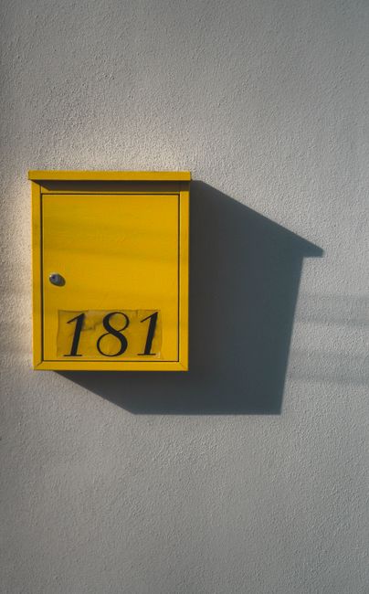 Close-up of a yellow mailbox with number 181 casting a shadow on a white wall in Miami, FL.