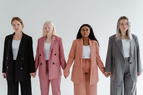 Free Four diverse women in business suits holding hands against a white background, symbolizing unity. Stock Photo