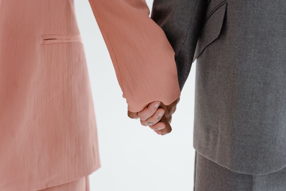 Close-up view of two people holding hands, wearing pink and grey suits, isolated on a white background.