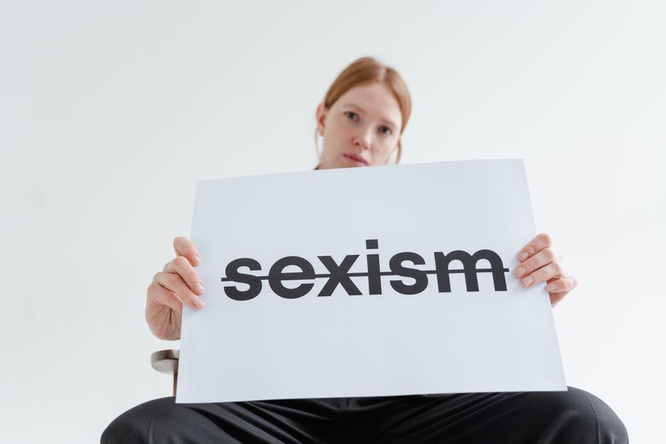 Una mujer caucásica sostiene con confianza un cartel que aborda el sexismo en un brillante ambiente de estudio.