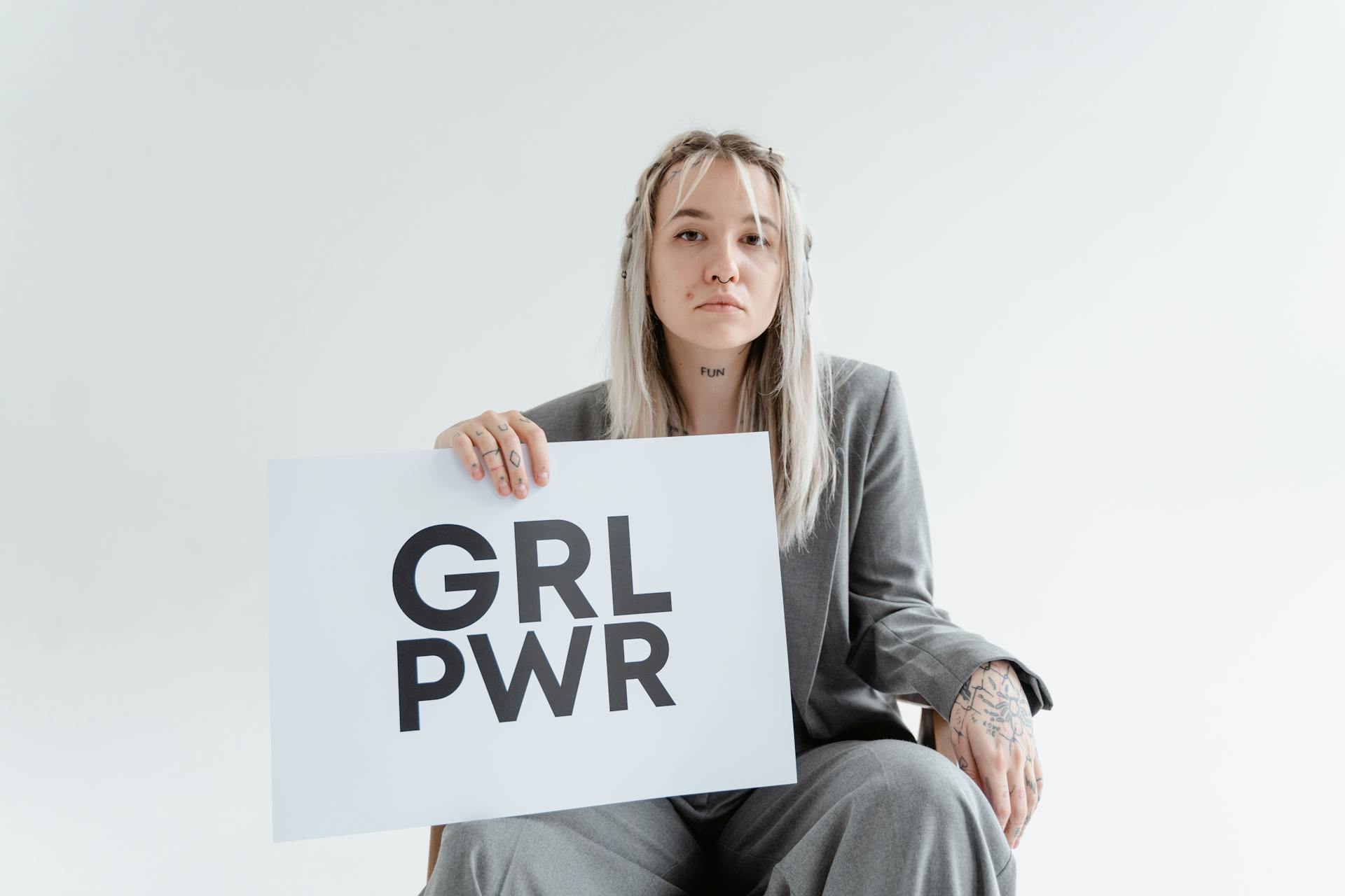 Confident woman showcases 'GRL PWR' sign, symbolizing empowerment and leadership indoors.