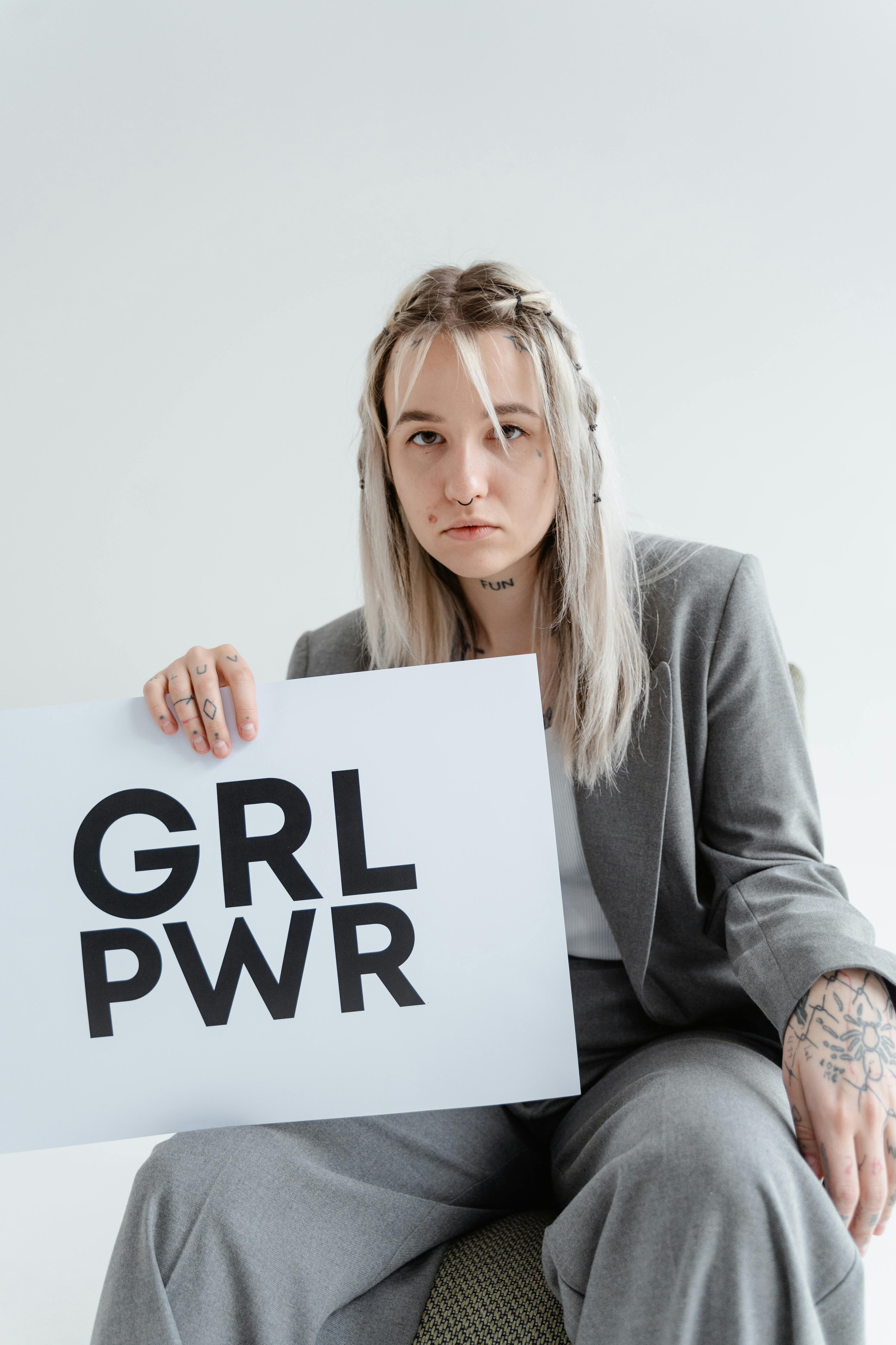 Portrait of a confident young woman in a gray blazer holding a 'GRL PWR' sign, symbolizing empowerment and strength.