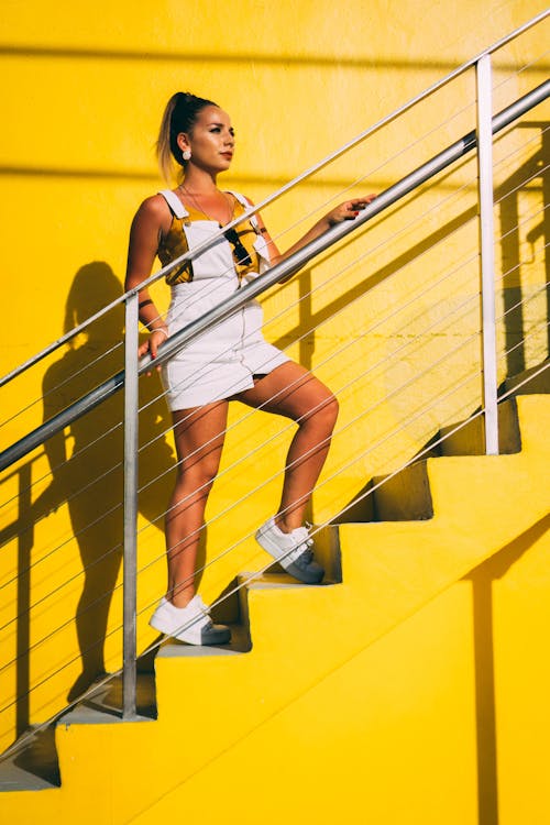 Woman in White Jumper Outfit Standing on Yellow Stairs