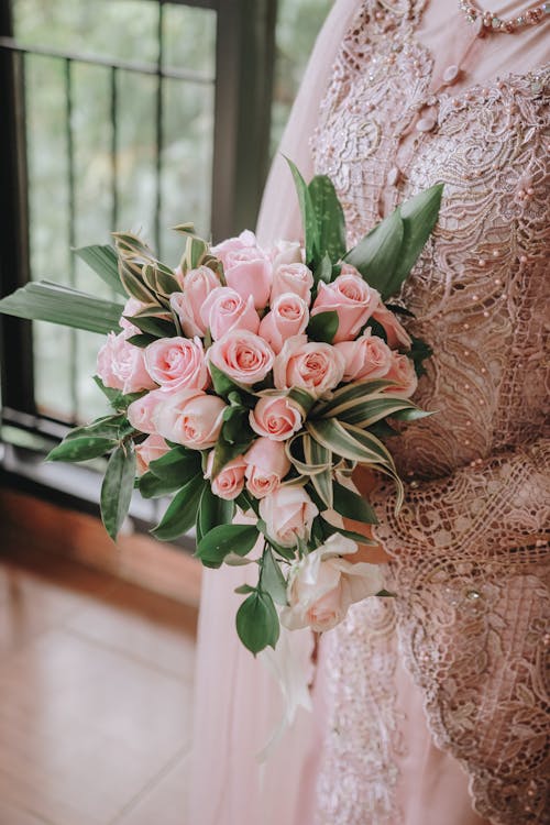 Faceless woman in dress with gentle lace and tender bouquet of fresh roses with pink petals in daytime