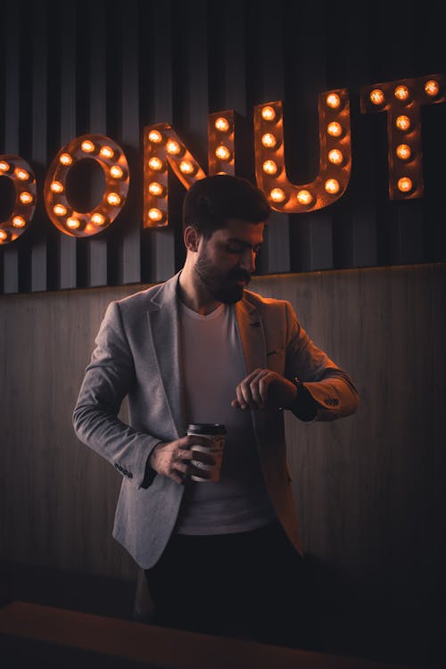 A Man in Gray Suit Holding a Cup of Coffee while Looking at His Watch