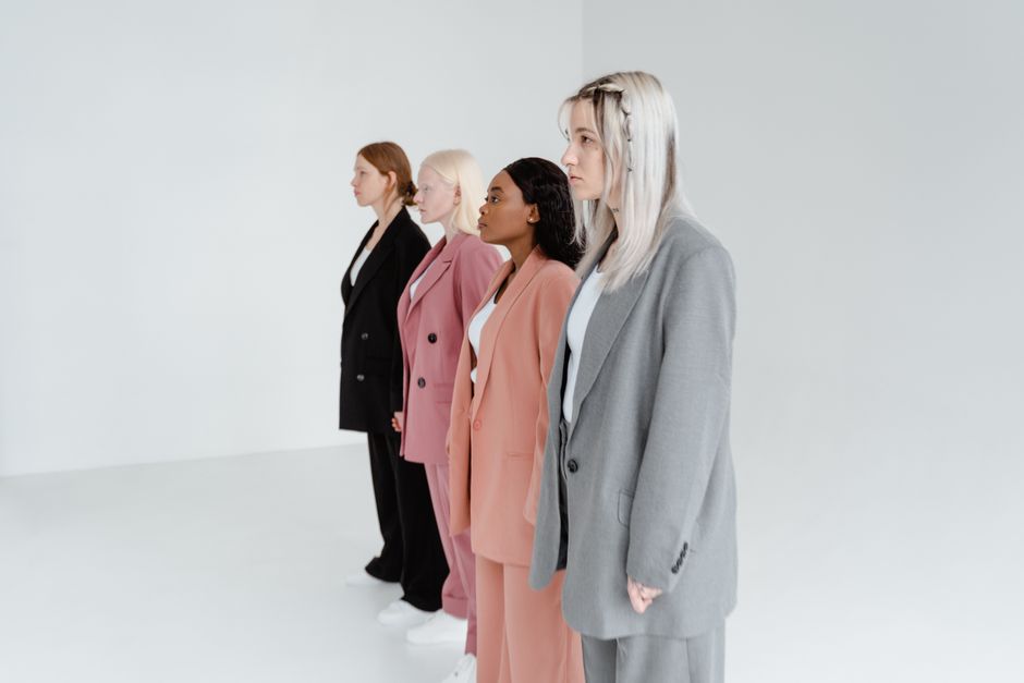 A group of diverse women wearing fashionable business suits in a minimalist studio setting.
