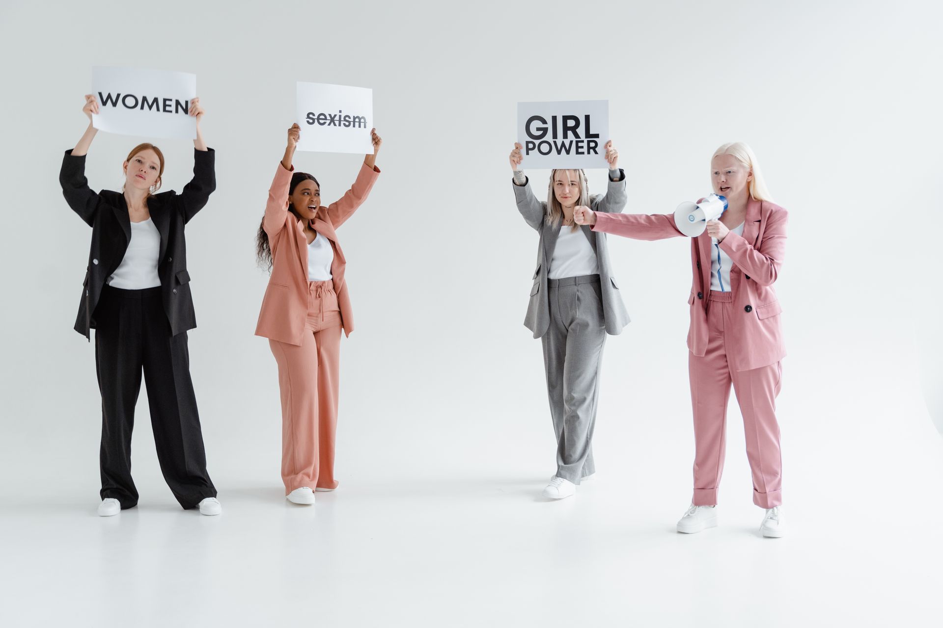 A group of women in business attire holding signs advocating for gender equality in a studio setting.