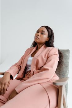 Confident African American woman posing in a stylish pink suit against a white background.
