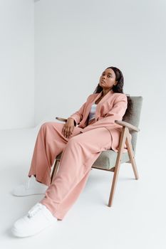 Fashion-forward woman in pink attire sitting on chair in minimal studio.