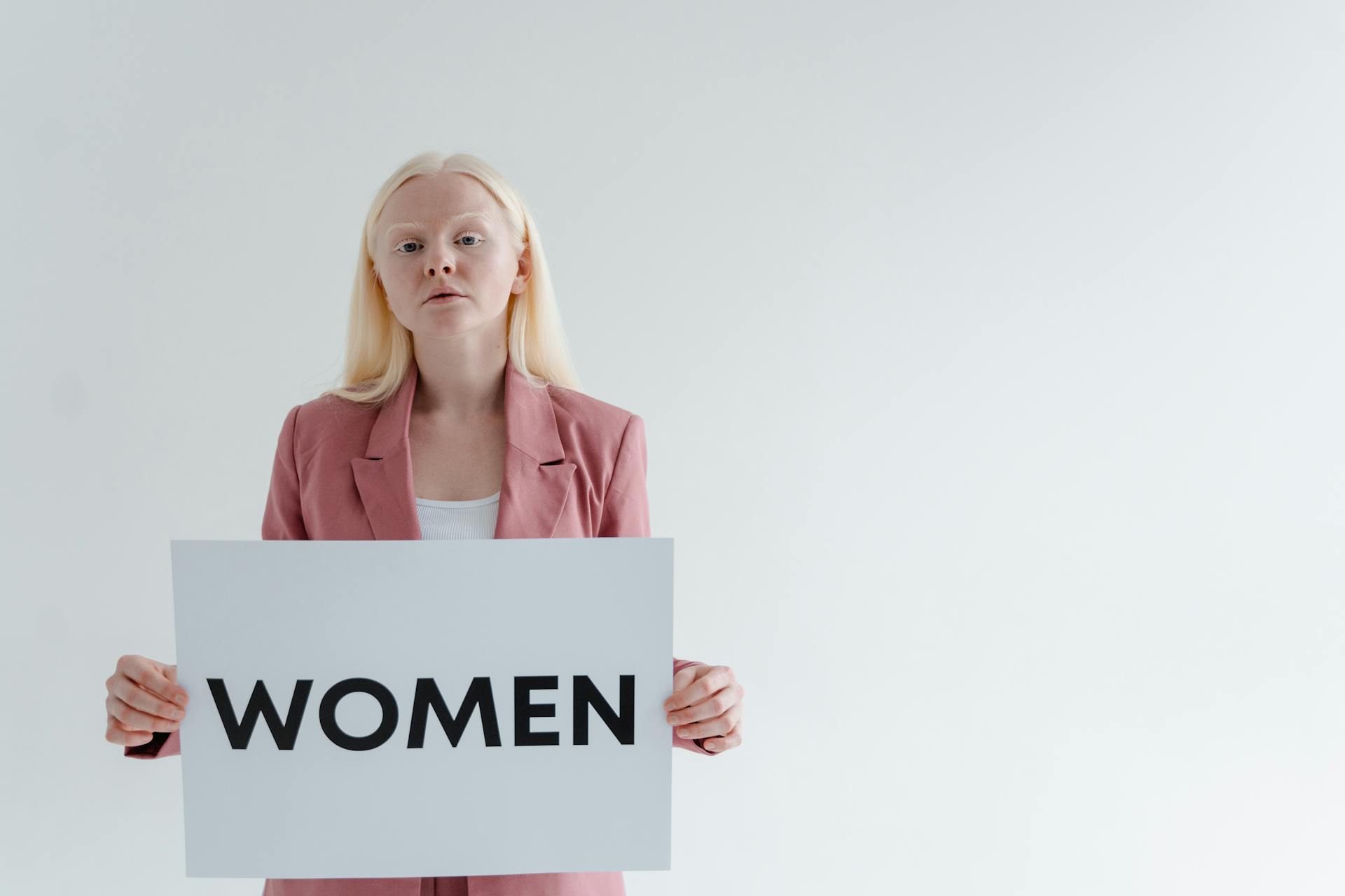 Woman in a Pink Blazer Holding a Card with the Word Women