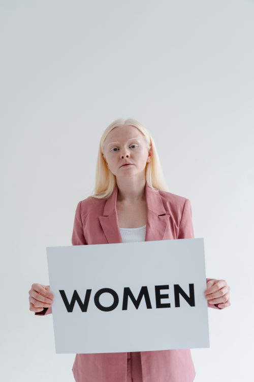 Free Empowered woman in a pink blazer confidently holds a sign reading 'Women' against a white background. Stock Photo