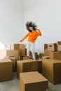 Joyful female with moving hair dancing among piles of carton containers after renting house on light background