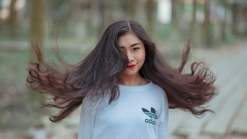 Free Young woman outdoors with flowing hair and playful pose in a white shirt. Stock Photo