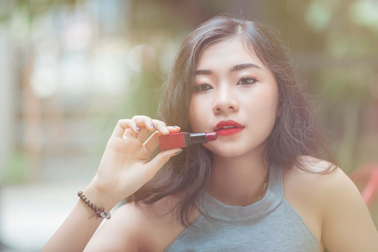 Woman in a gray halter-neckline top holding red lipstick