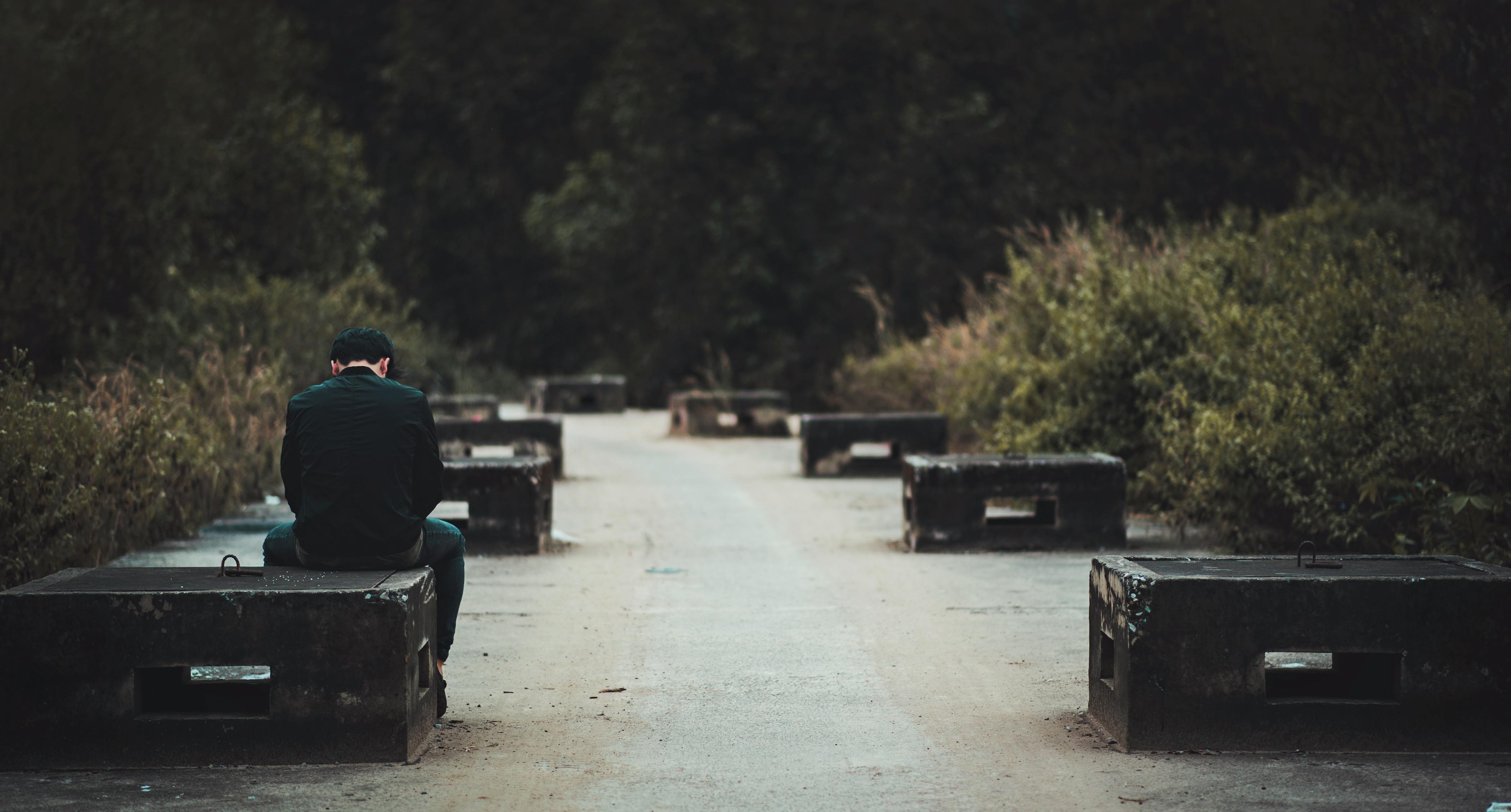 man in black dress shirt with blue denim shirt sitting on black concrete bench near green plants