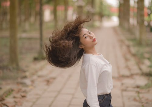 Ücretsiz Beyaz Ekip Yaka Uzun Kollu Gömlekli Kadın Yolda Ortada Saçlarını Sallayarak Portre Fotoğrafı Stok Fotoğraflar