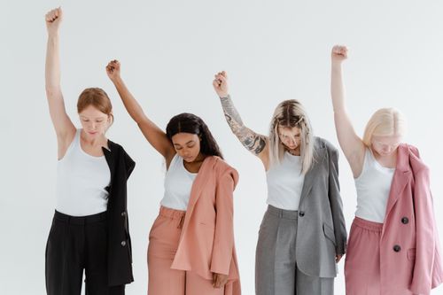 Free Four diverse women in corporate attire raise their arms in empowerment on a white background. Stock Photo