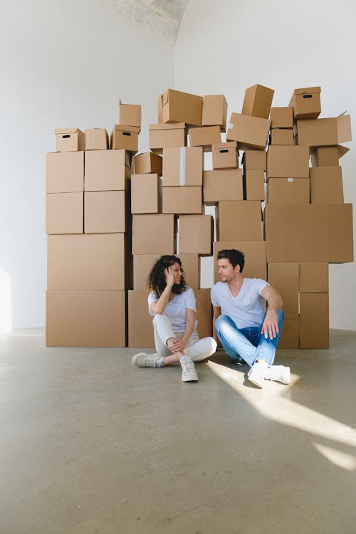 Free Woman touching face against boyfriend with crossed legs while looking at each other on floor with carton boxes in house Stock Photo