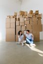 Woman touching face against boyfriend with crossed legs while looking at each other on floor with carton boxes in house