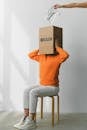 Crop anonymous person putting creased paper with Rubbish inscription in container with Brain title on head of female on chair