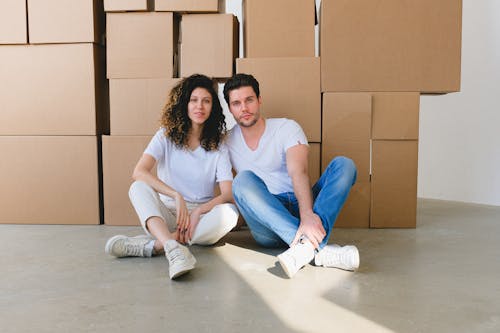 Couple with crossed legs against carton containers during relocation