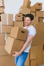 Cheerful bearded male with closed eyes in t shirt and jeans carrying cardboard containers after moving into new house