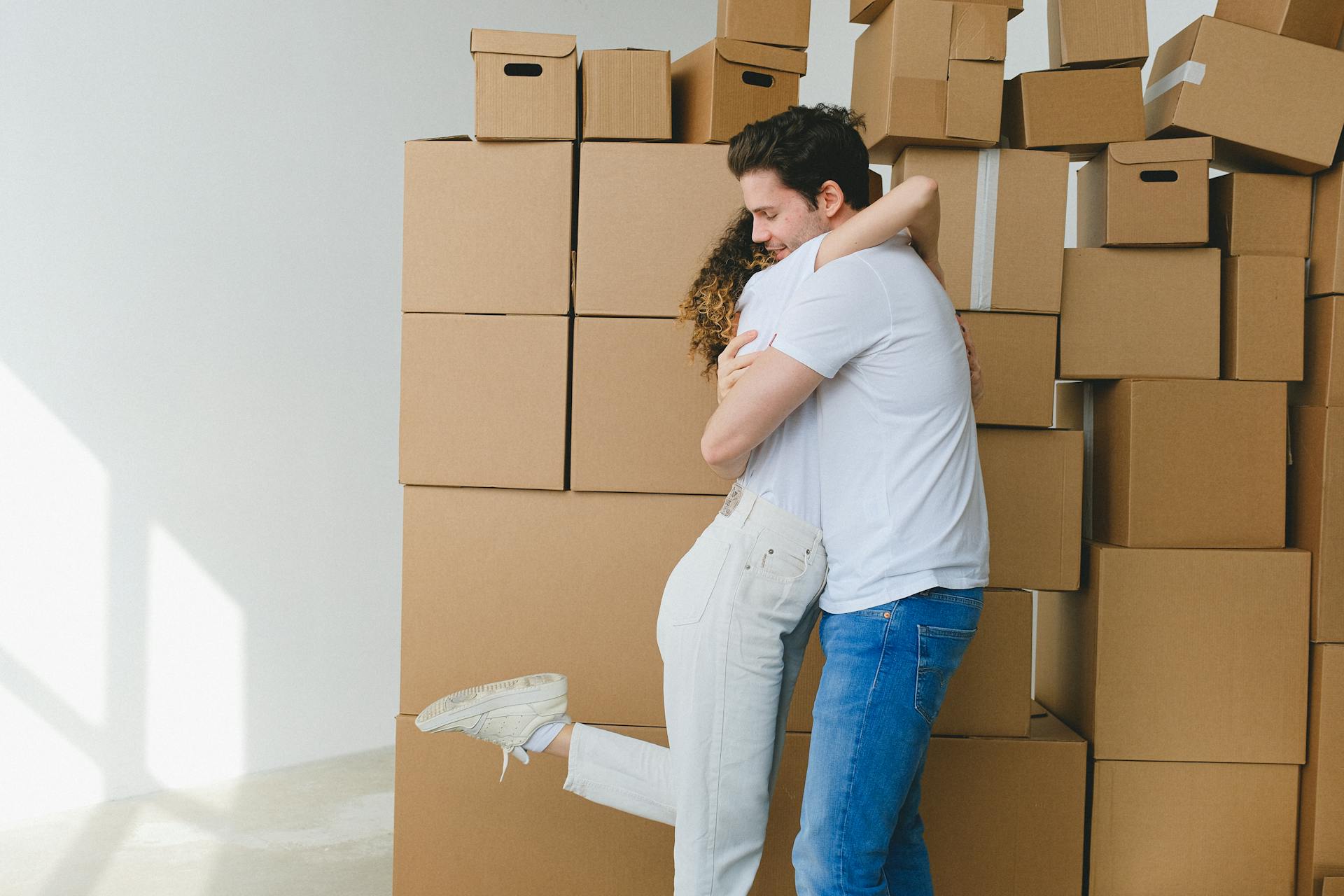 Cheerful couple hugging near carton boxes during relocation in new apartment