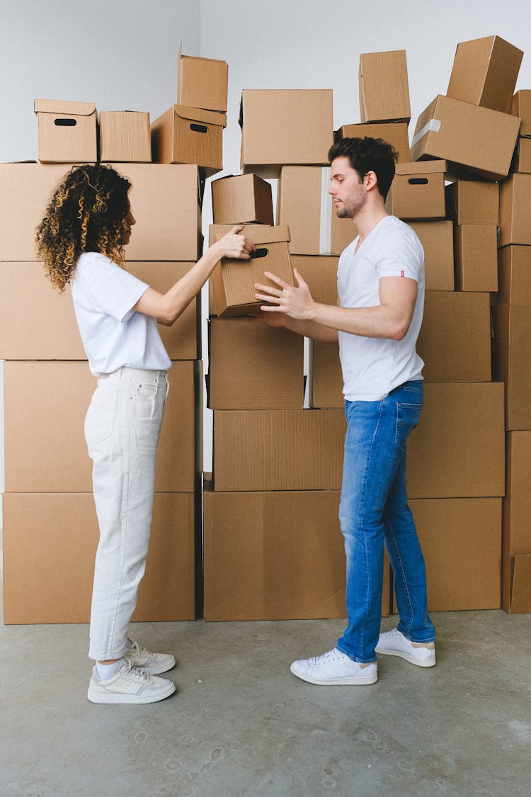 Young Couple Carrying Carton Boxes In New Flat During Relocation