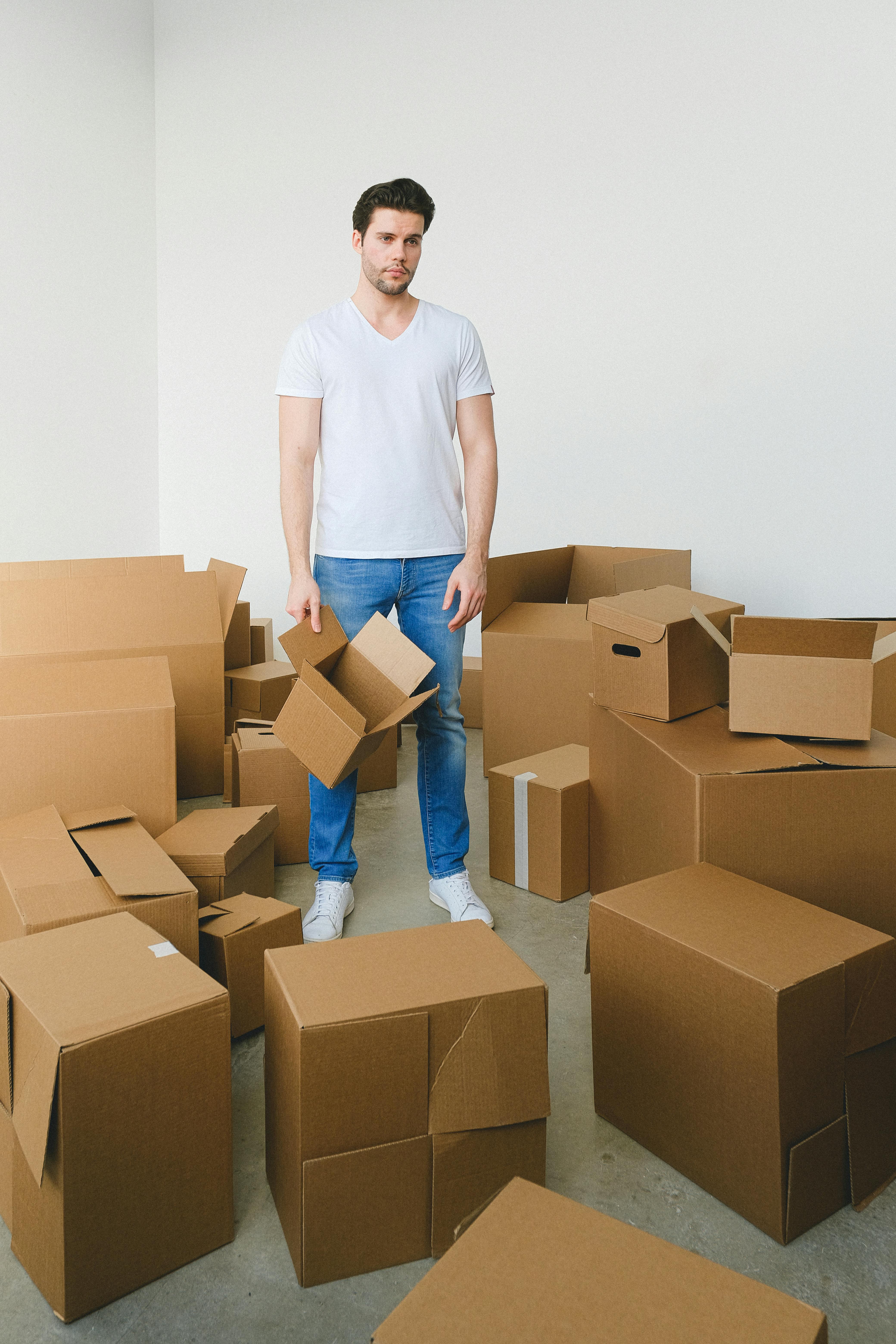 thoughtful guy standing near stack of boxes after moving in new apartment
