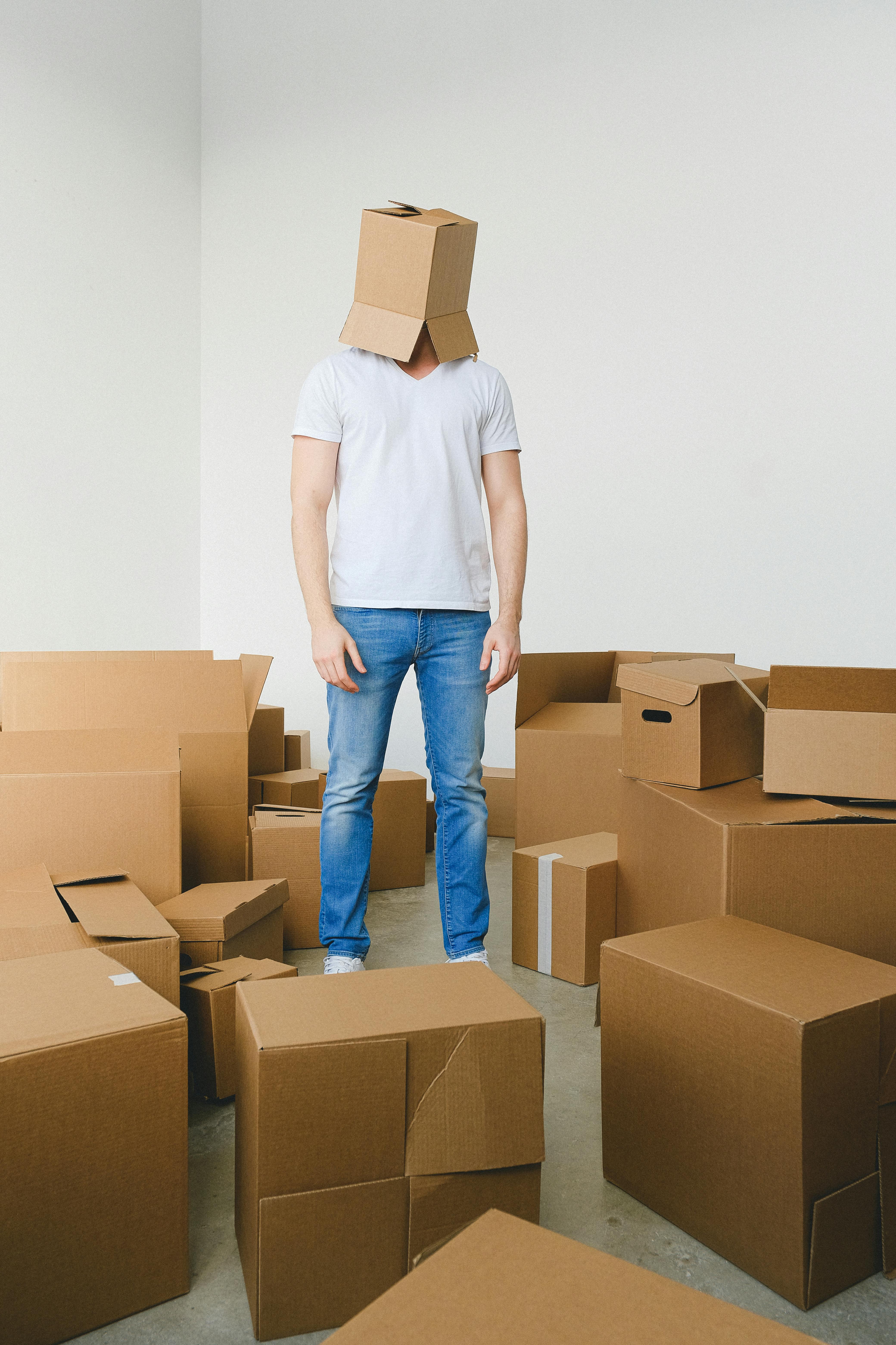 tired male with carton box on head standing in room before relocation