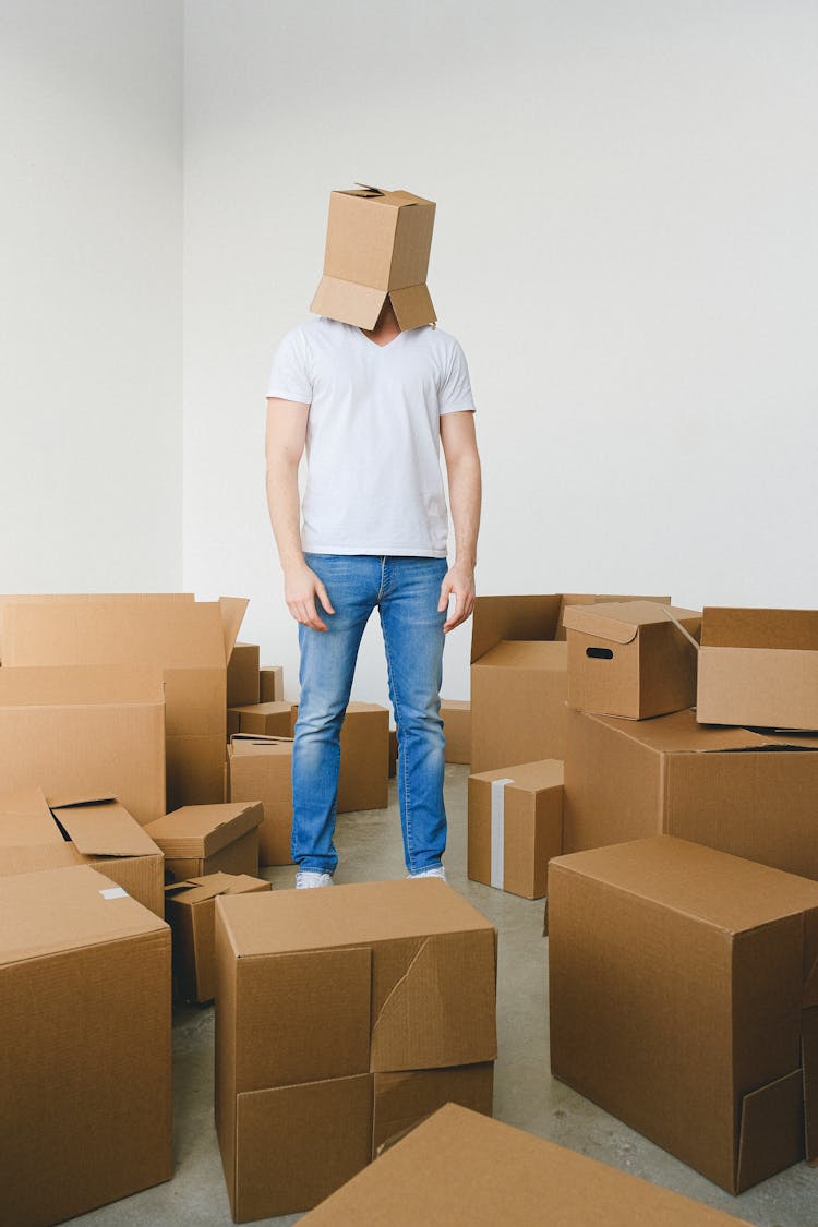 Tired Male With Carton Box On Head Standing In Room Before Relocation