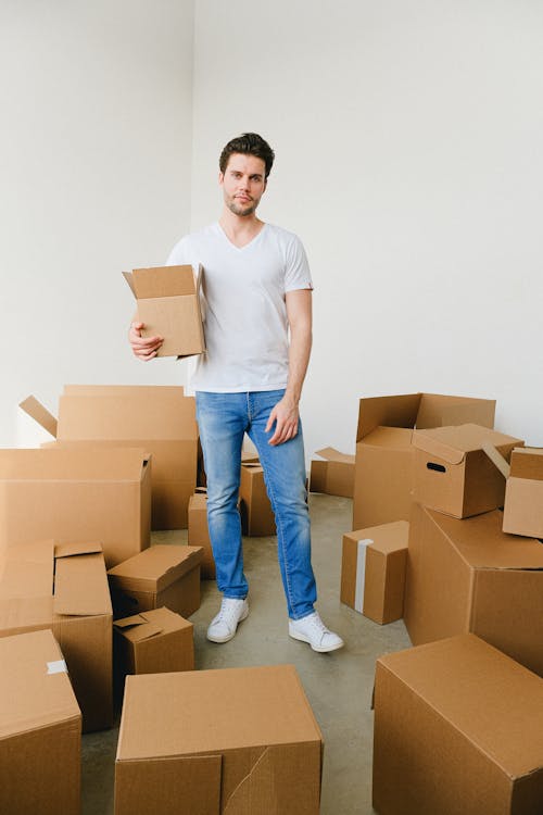 Content relocating man standing amidst boxes and looking at camera