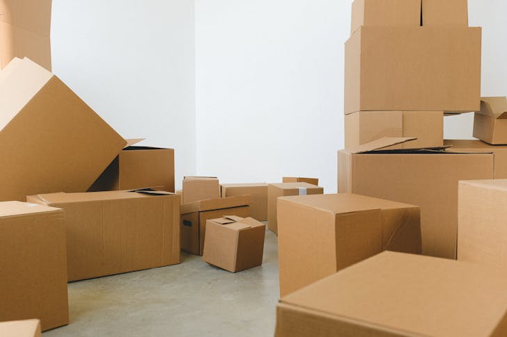 Stack of carton boxes of various shapes and sizes scattered in floor near white walls during relocation
