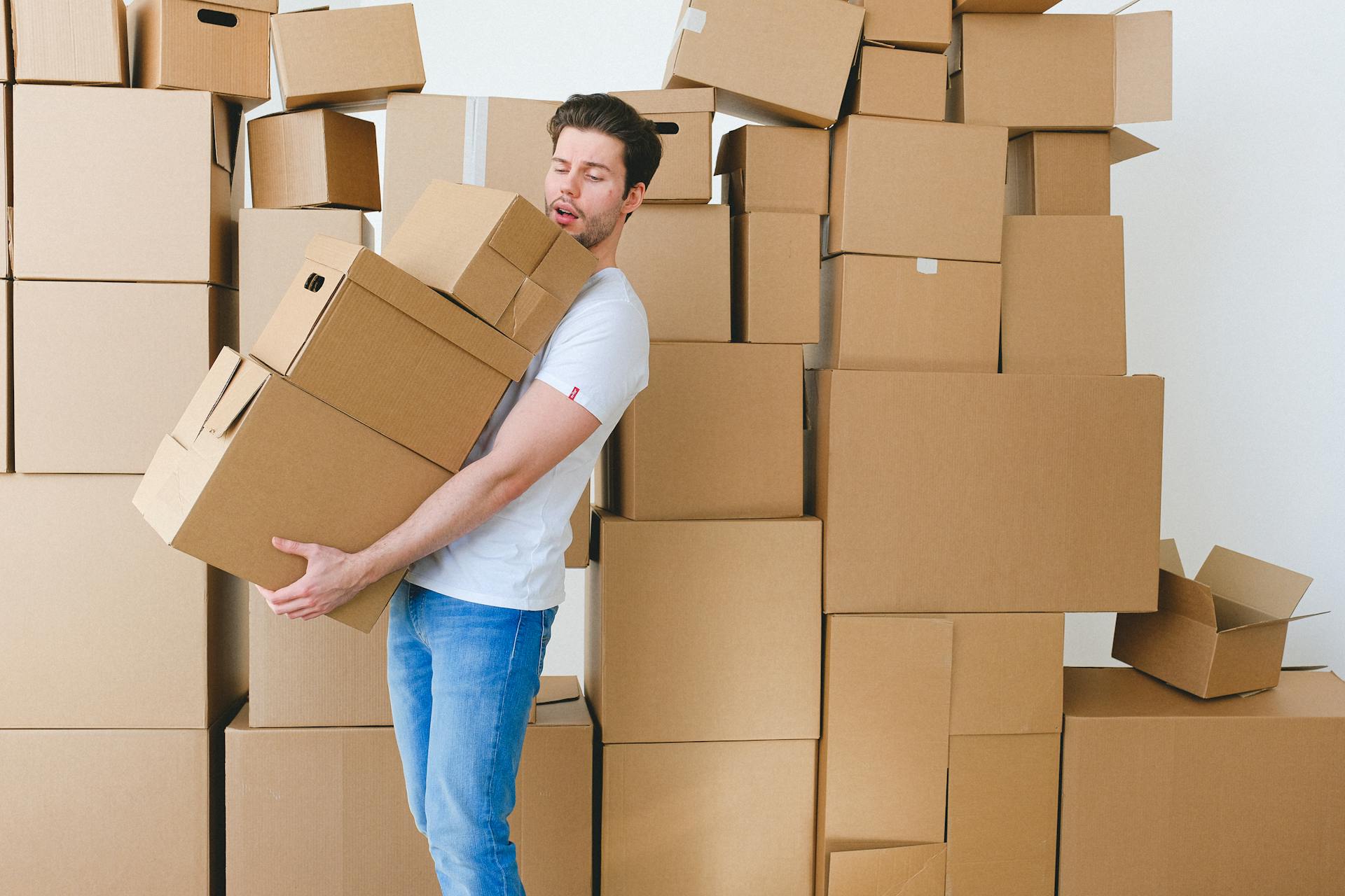 Young man carrying heap of cardboard boxes during relocation in new flat