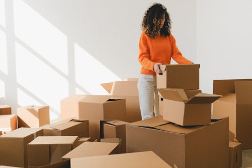 Focused young female with curly dark hair in casual outfit arranging pile of cardboard boxes while preparing for relocation in new apartment