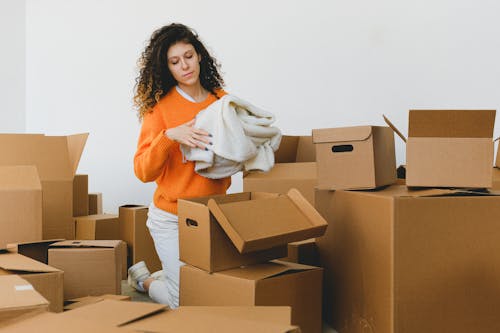 Free Focused young relocating female packing belonging into cardboard boxes Stock Photo