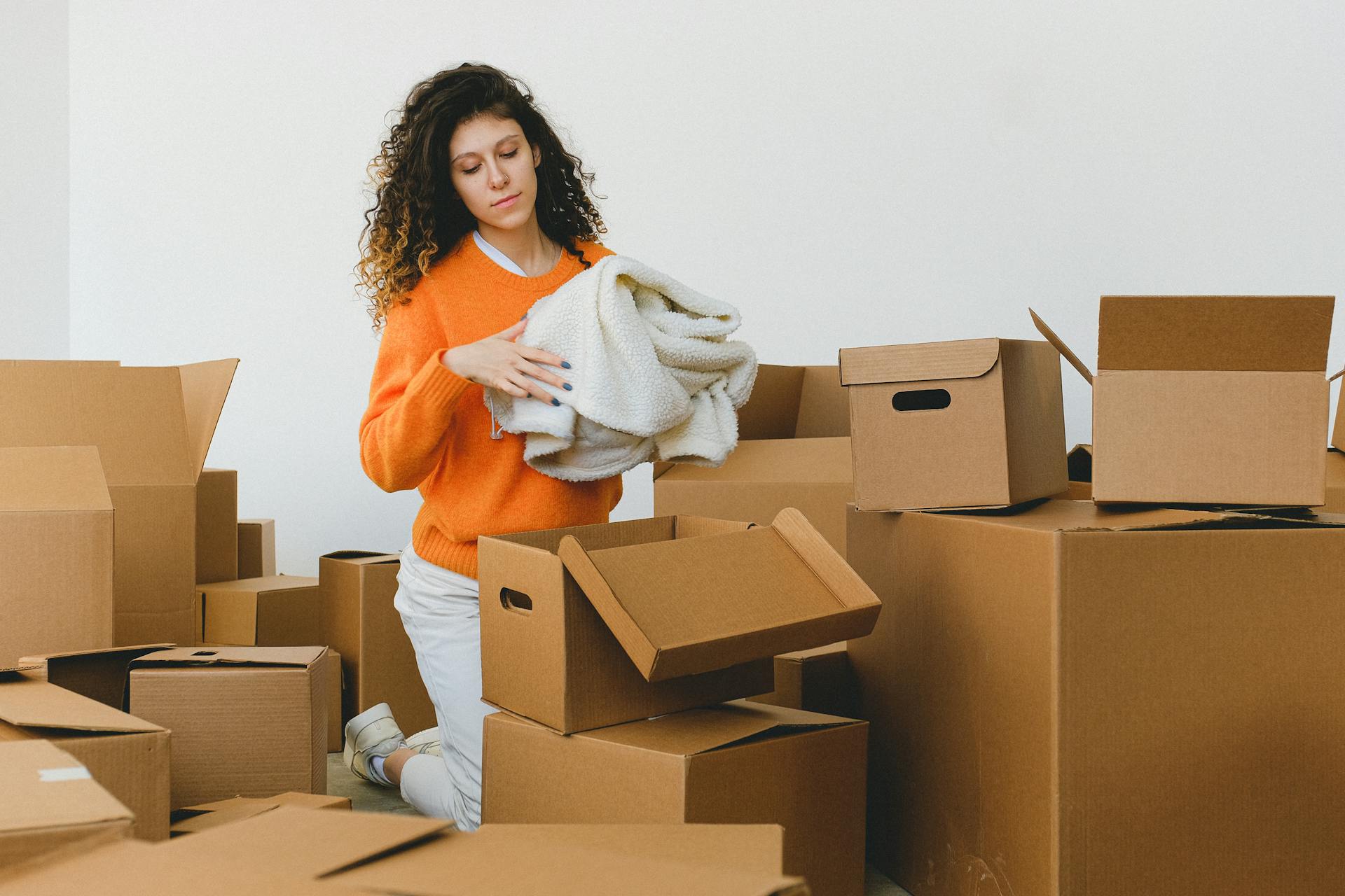 Focused young relocating female packing belonging into cardboard boxes