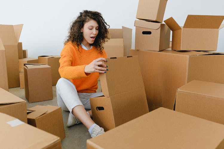 Surprised Young Woman Opening Cardboard Box After Delivering Parcel