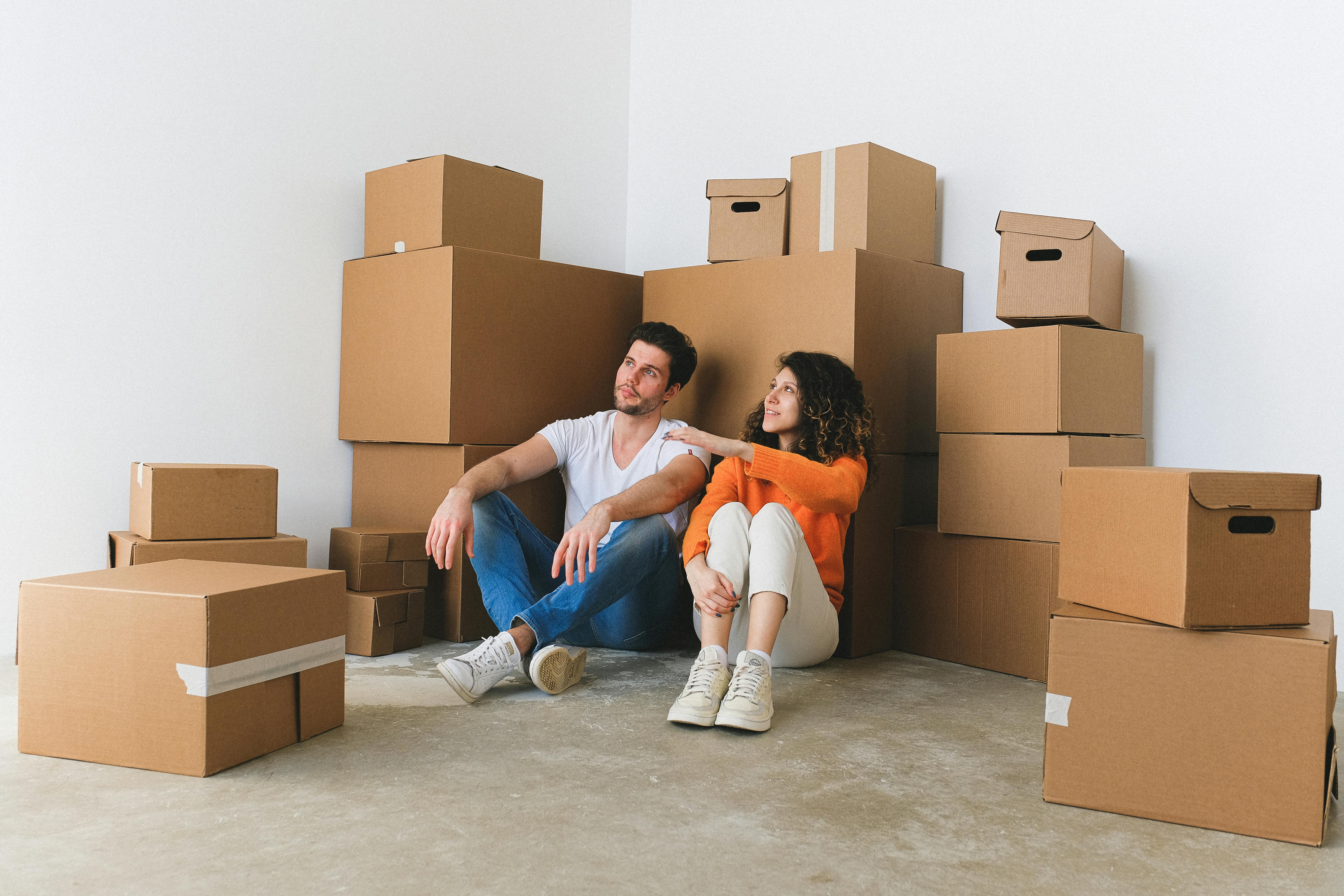 content young couple talking while sitting on floor near cardboard boxes after relocation