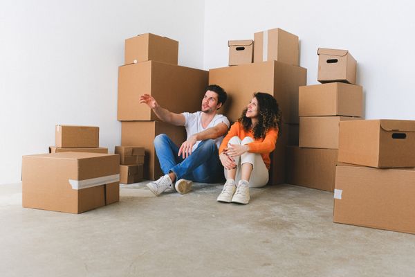 Couple sitting among moving boxes planning where everything goes while merging two households