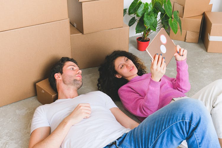 Loving Young Couple Lying On Floor And Looking At Framed Photo After Relocation