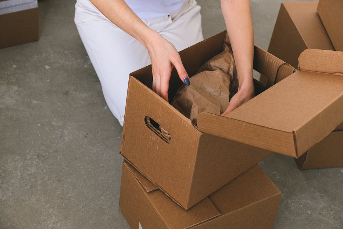 Crop faceless woman packing belongings into cardboard box before relocation