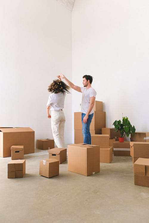 Full body of romantic young couple in casual dancing in new purchased flat amidst pile of carton boxes after relocation