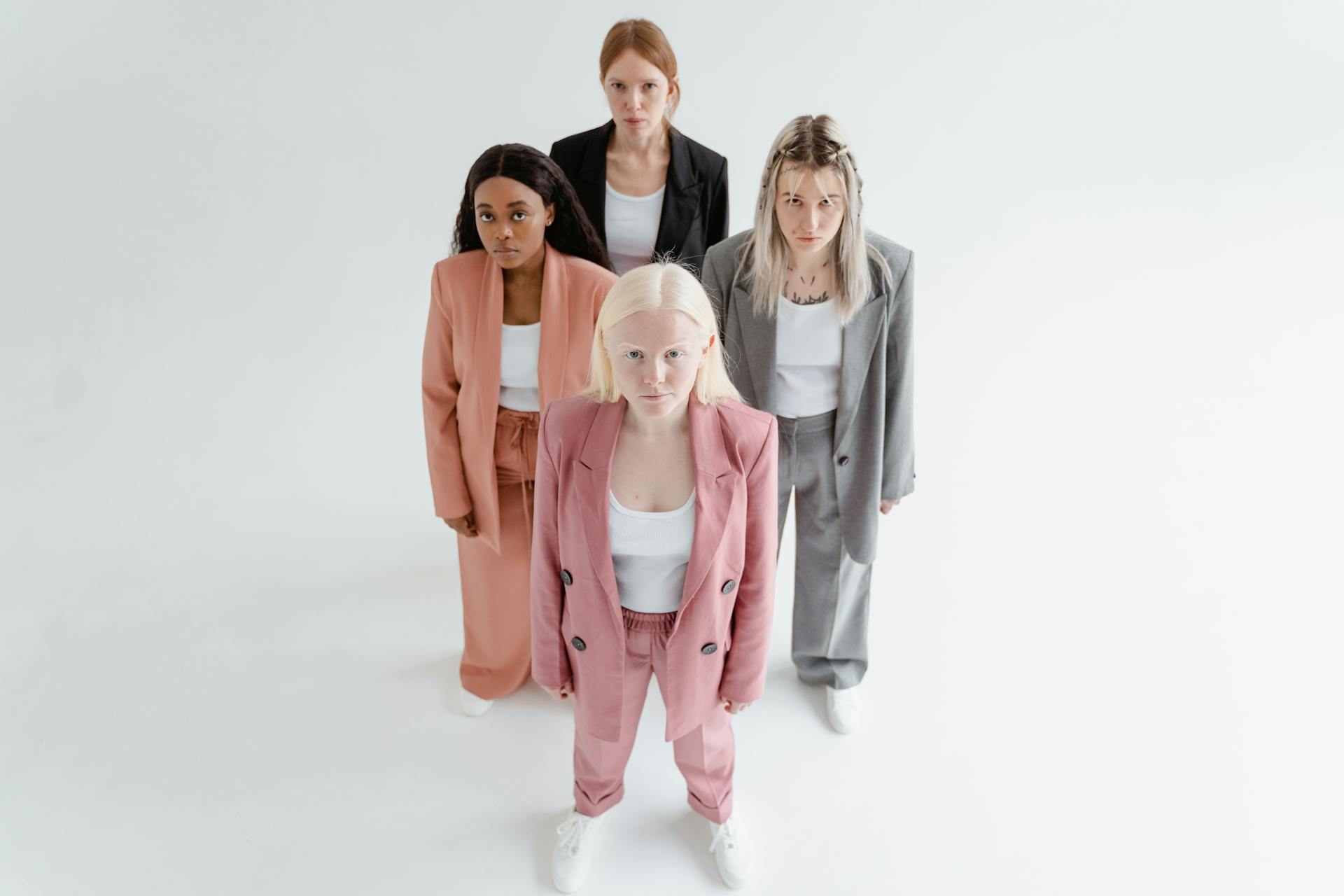 Four women in stylish suits standing on a white background, showcasing diversity and confidence.