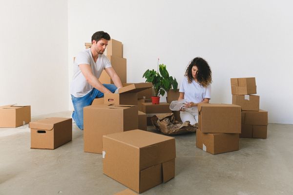 Couple unpacking cardboard moving boxes in an empty room, deciding what to unpack first after moving