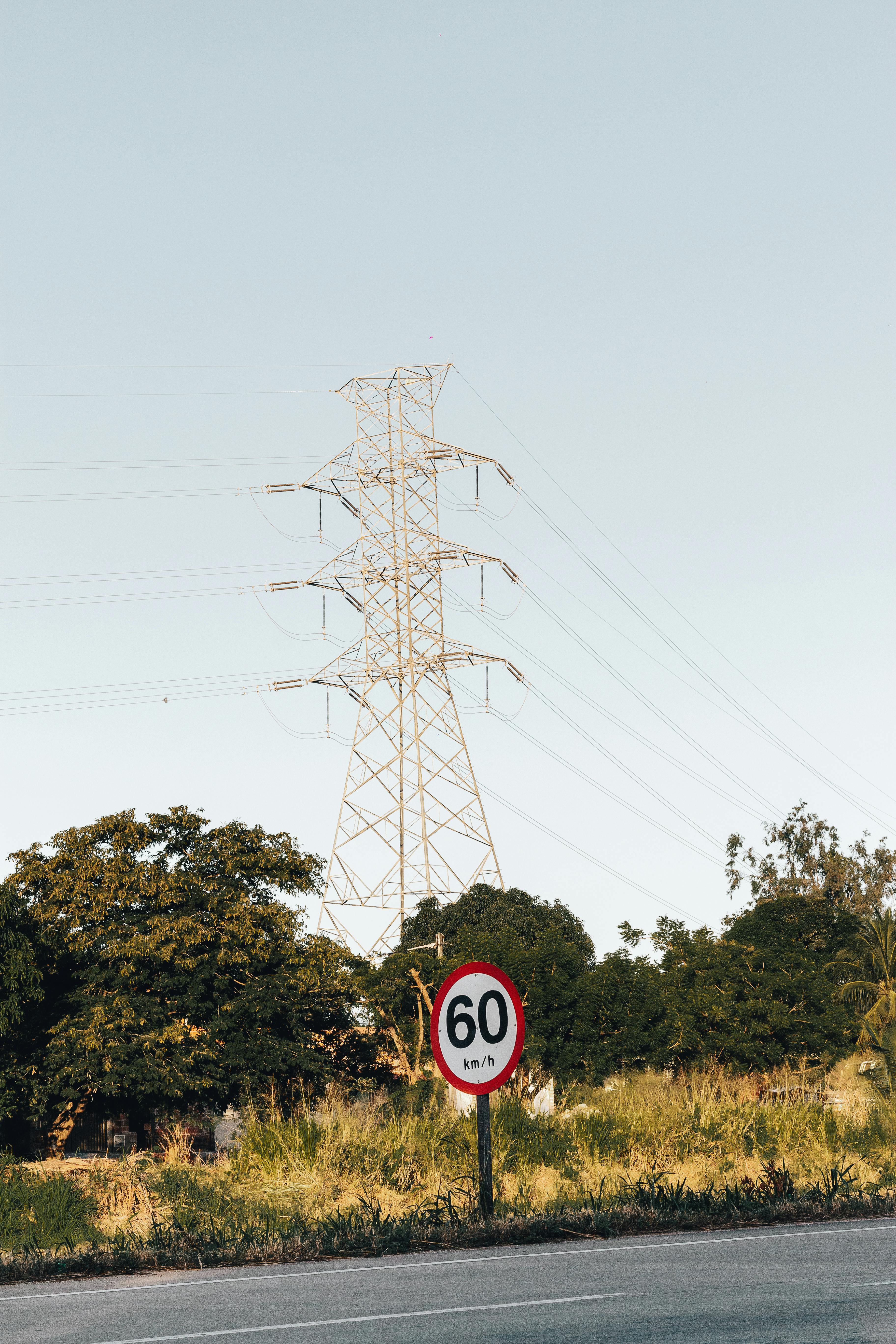 A transmission tower stands over a rural road with a 60 km/h speed limit sign.