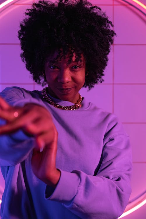 Positive African American female in sweatshirt smiling and looking at camera in violet bright light