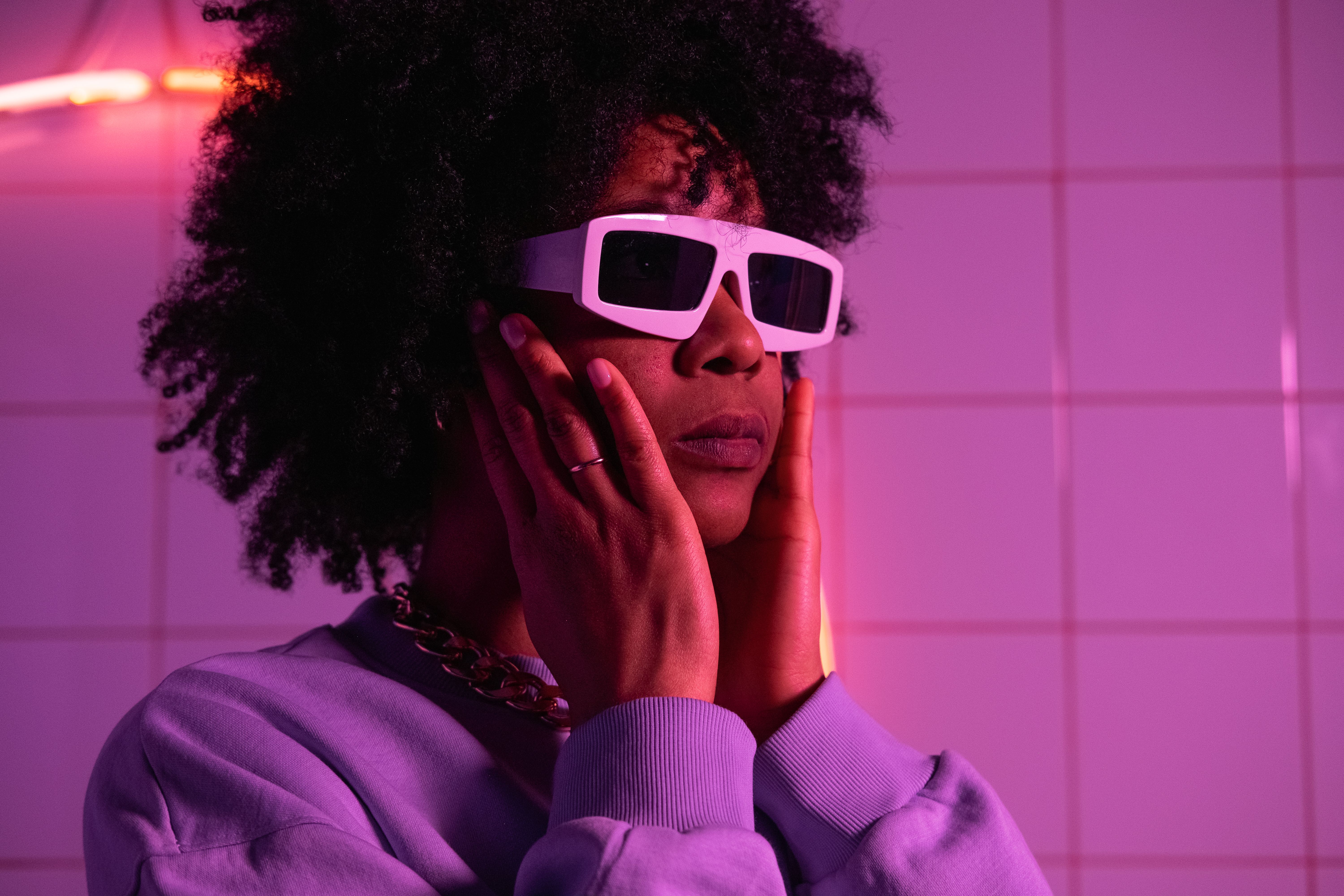 Extravagant crop African American female in sweatshirt looking away in ultraviolet light near ceramic tile
