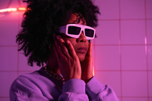 Extravagant crop African American female in sweatshirt looking away in ultraviolet light near ceramic tile
