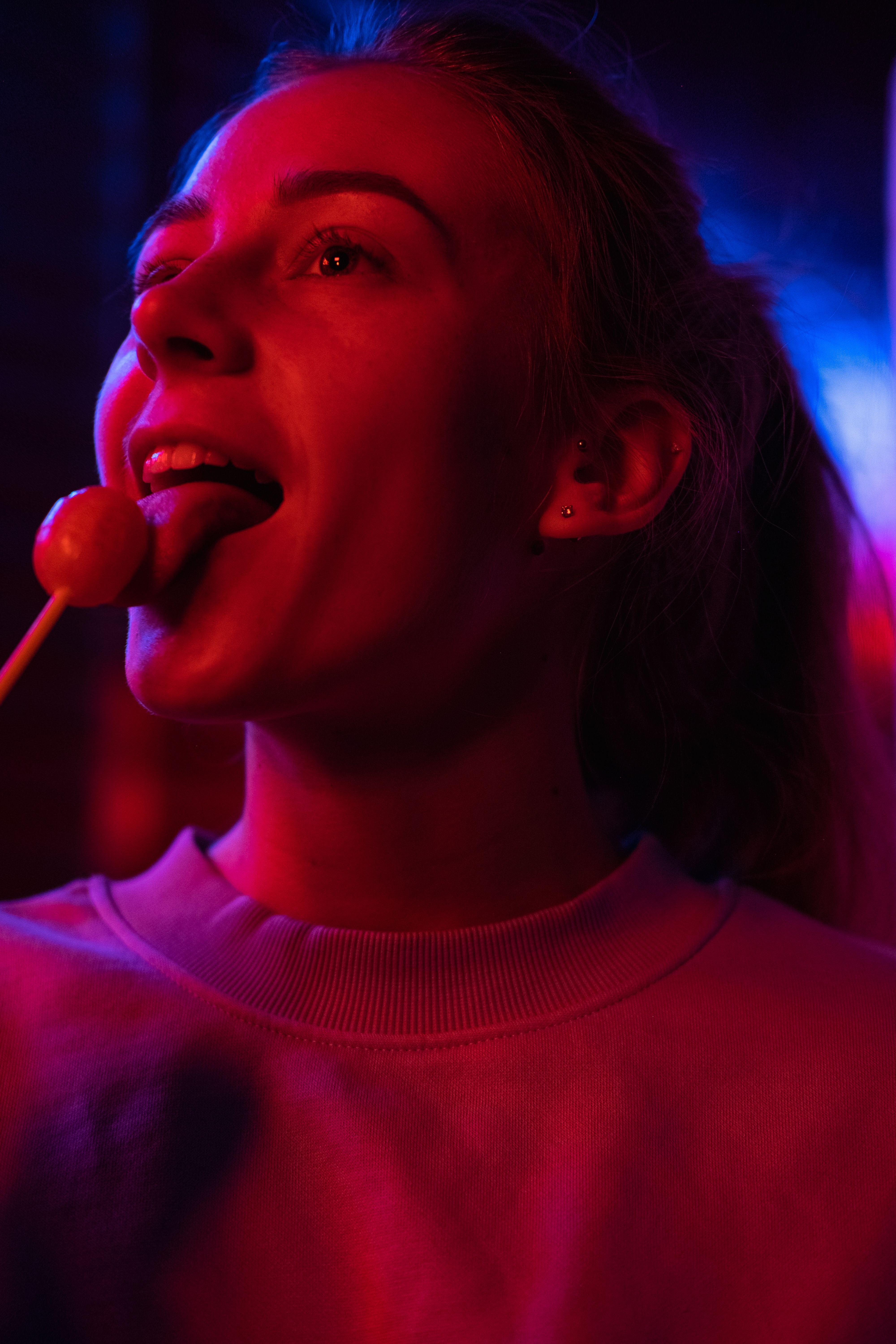 Glad female eating sweet delicious lollipop and smiling on blurred background in dim ultraviolet light
